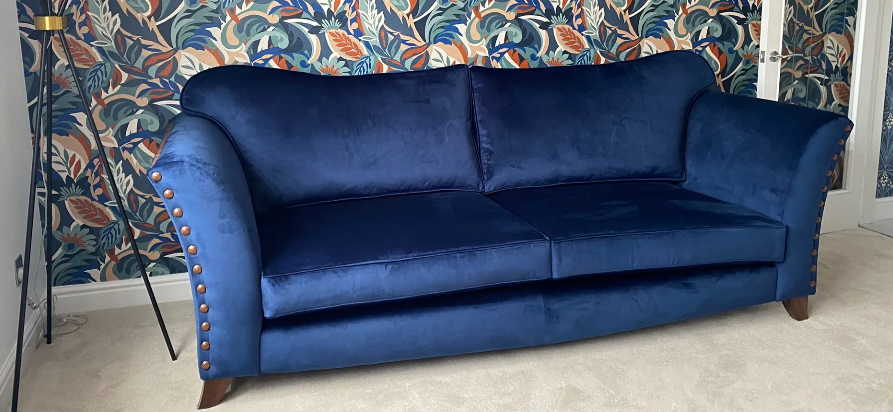 Elegant blue velvet couch set before a colorful floral wallpaper design.