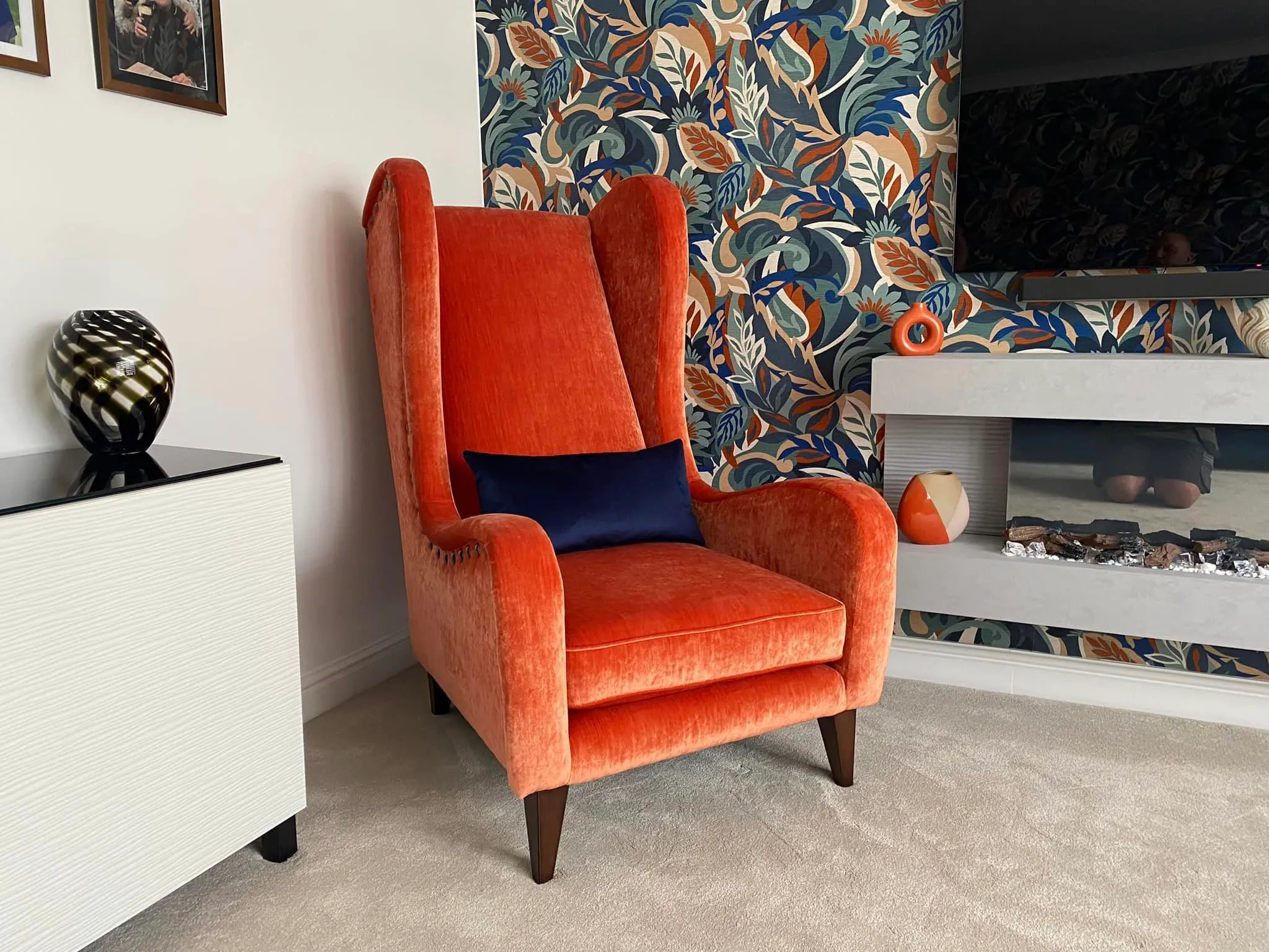 A vibrant orange chair set before a crackling fireplace, enhancing the room's warmth and comfort.