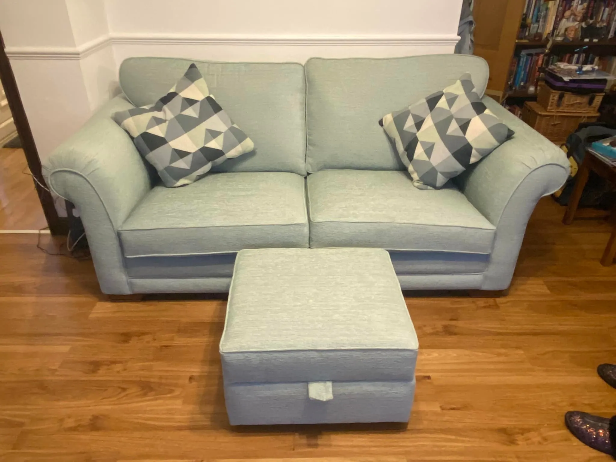 A recently re-upholstered couch alongside an ottoman on a warm hardwood floor, enhancing the room's comfort and aesthetic appeal.